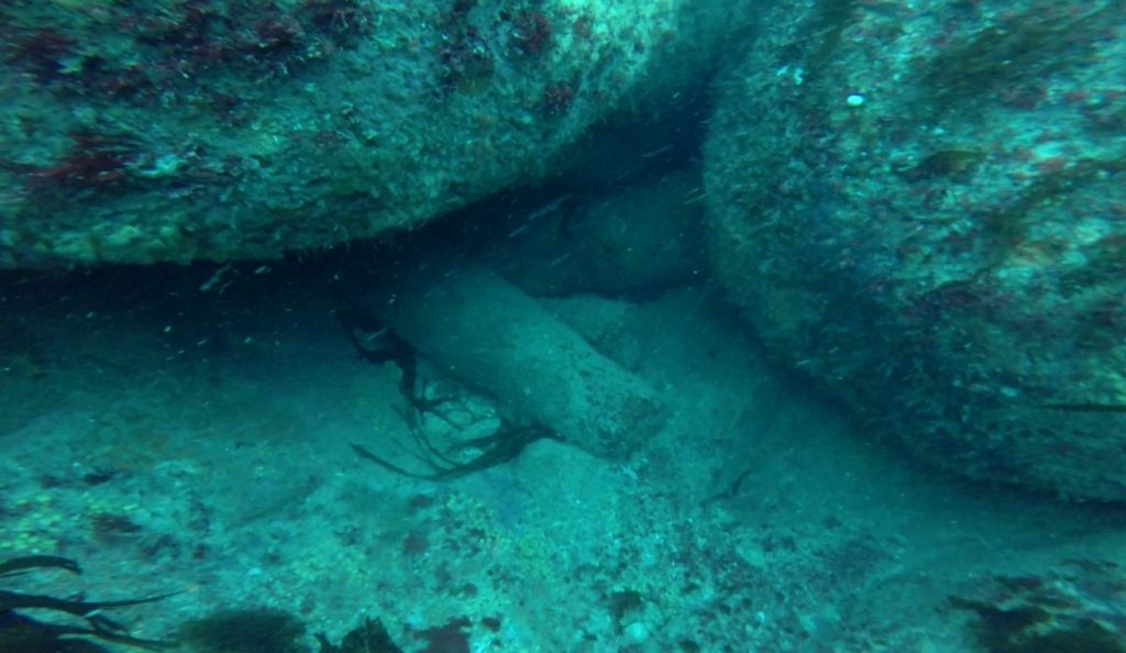 Rocky seabed, with the muzzle of a worn iron cannon sticking out from beneath a large boulder