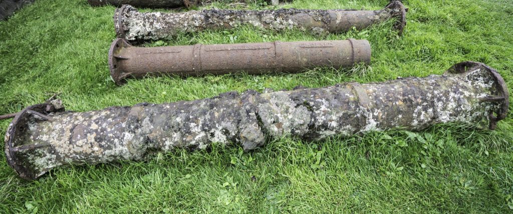 Three large cast iron pipe sections lying on the grass at East Pool Mine in Cornwall