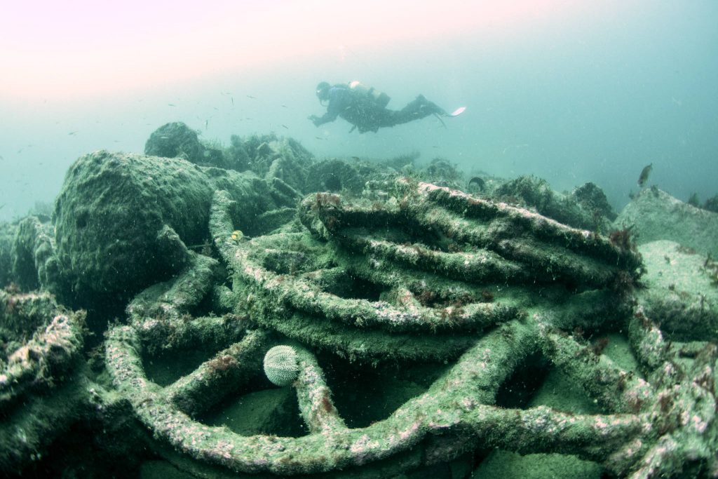 A diver swims over the pile of iron wheels on the seabed