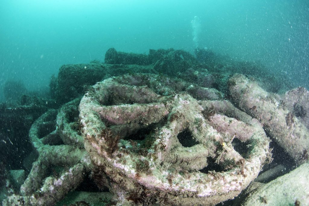 Six-spoked iron wheel sitting on top of several similar wheels on the seabed