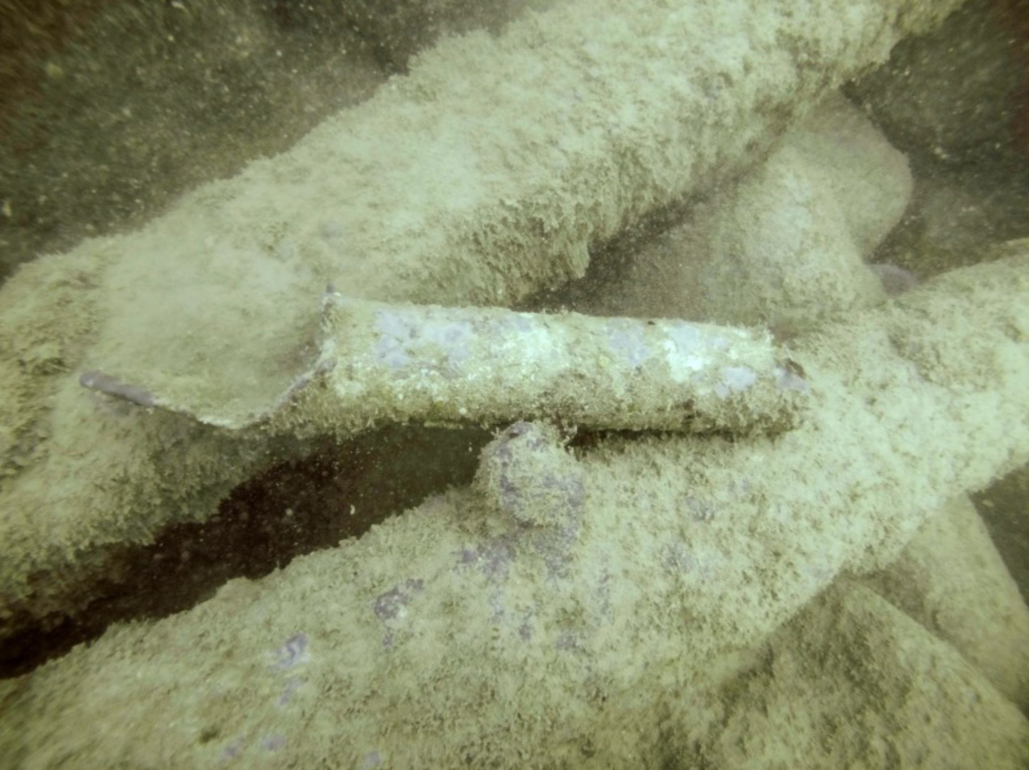 Underwater photograph of a lead scupper (O7). The scupper is 0.33m long and 0.06m in diameter – the iron pipes it is  sitting on are the socketed pipes of the cargo mound